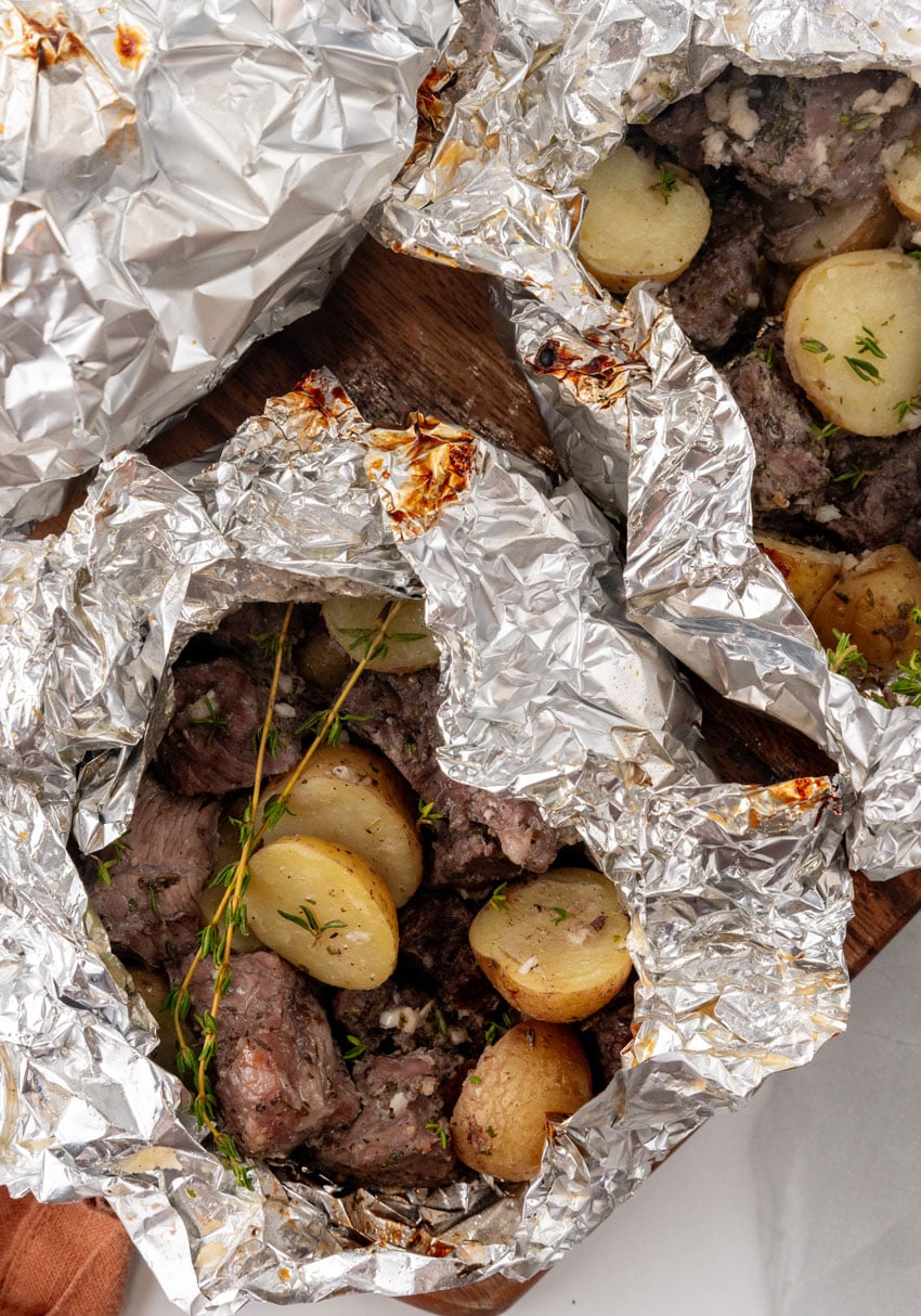 an opened garlic butter grilled steal and potato foil packet resting on a wooden cutting board