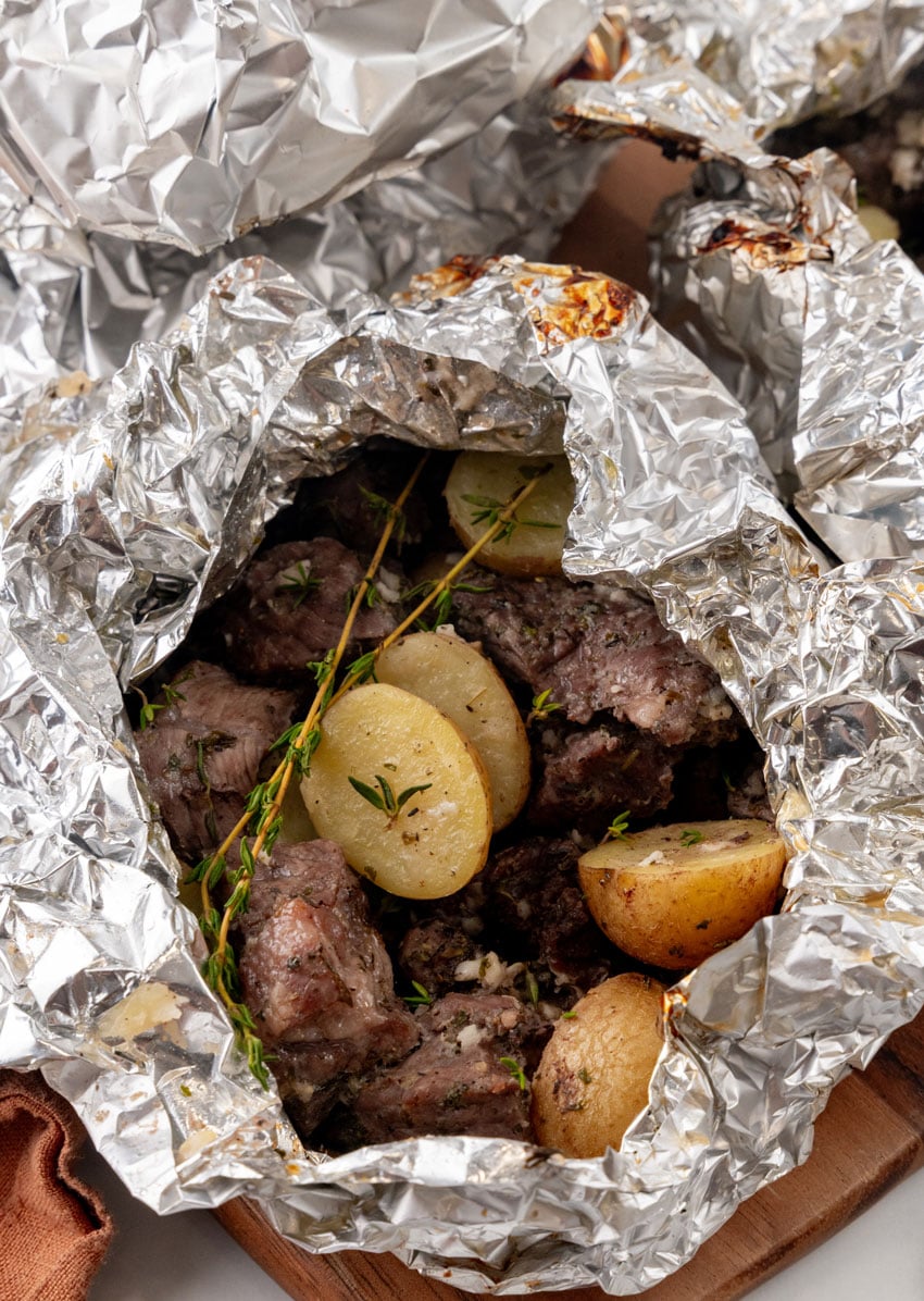 an opened garlic butter grilled steal and potato foil packet resting on a wooden cutting board