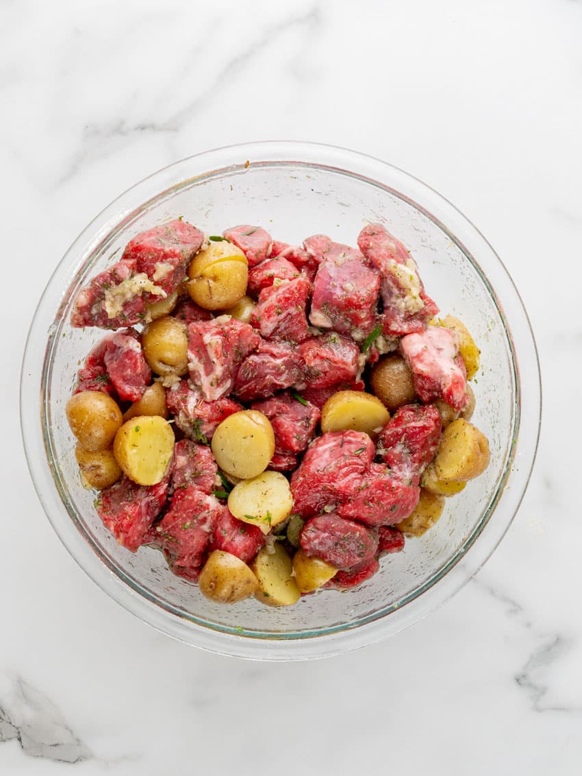 chunks of steak and quartered potatoes mixed with garlic and butter in a glass mixing bowl