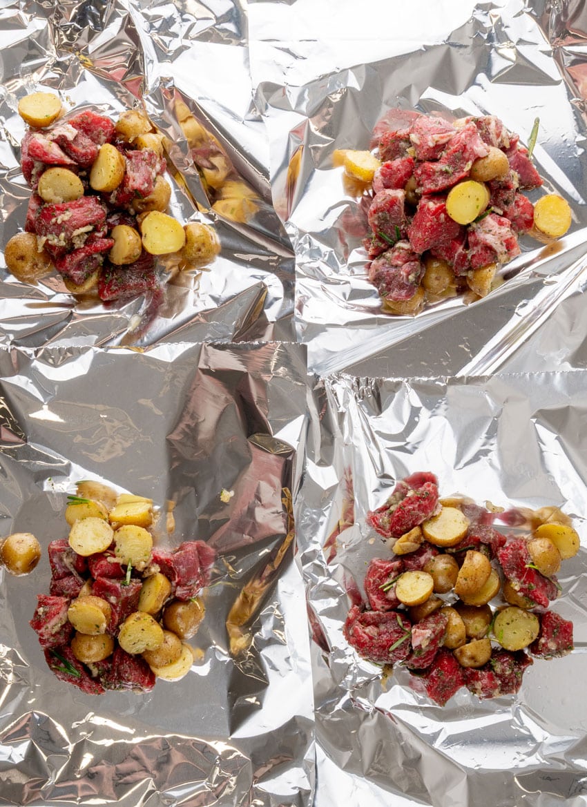 chunks of steak and quartered potatoes on sheets of aluminum foil
