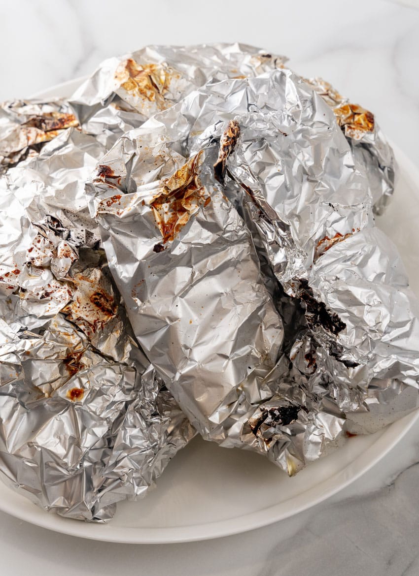 grilled steak and potato foil packets resting on a white plate