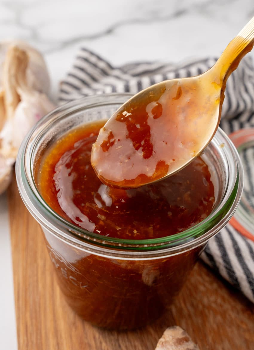 a spoon scooping homemade teriyaki sauce out of a small glass jar