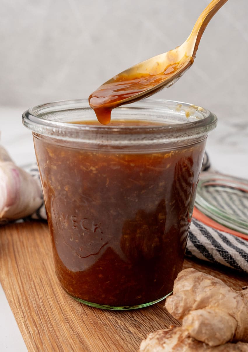 a spoon scooping homemade teriyaki sauce out of a small glass jar