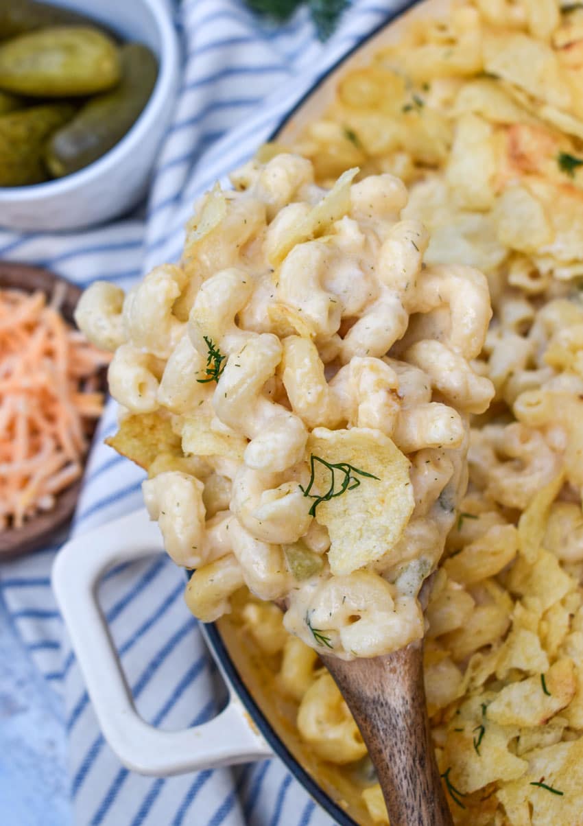 a wooden spoon holding up a scoop of creamy dill pickle mac and cheese