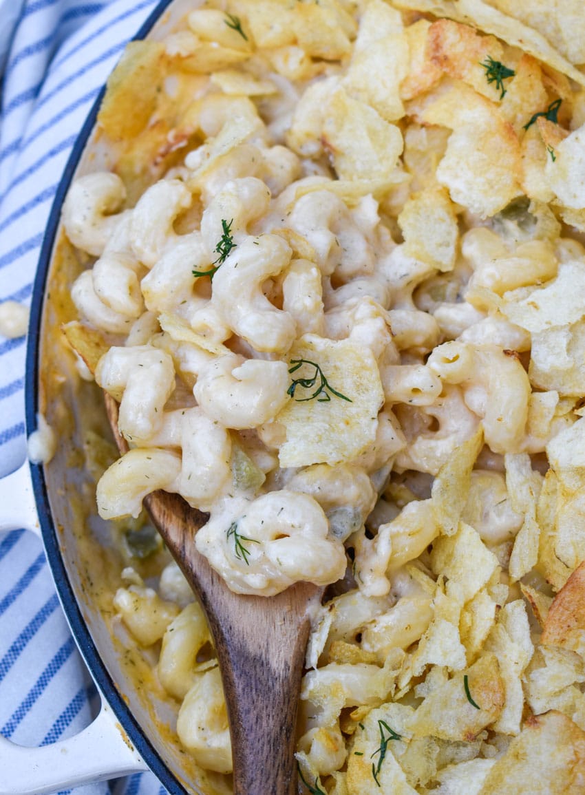 a wooden spoon scooping potato chip topped dill pickle mac and cheese out of a large skillet
