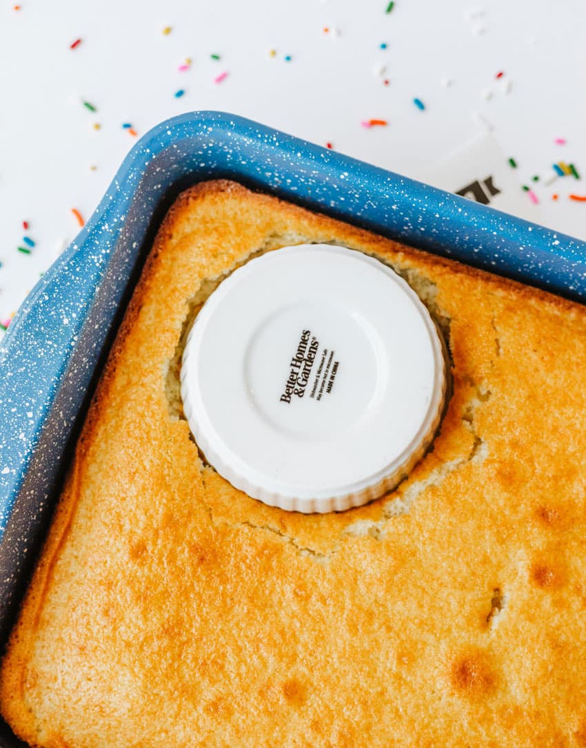 a white ramekin pressed into a baked yellow cake in a blue baking dish