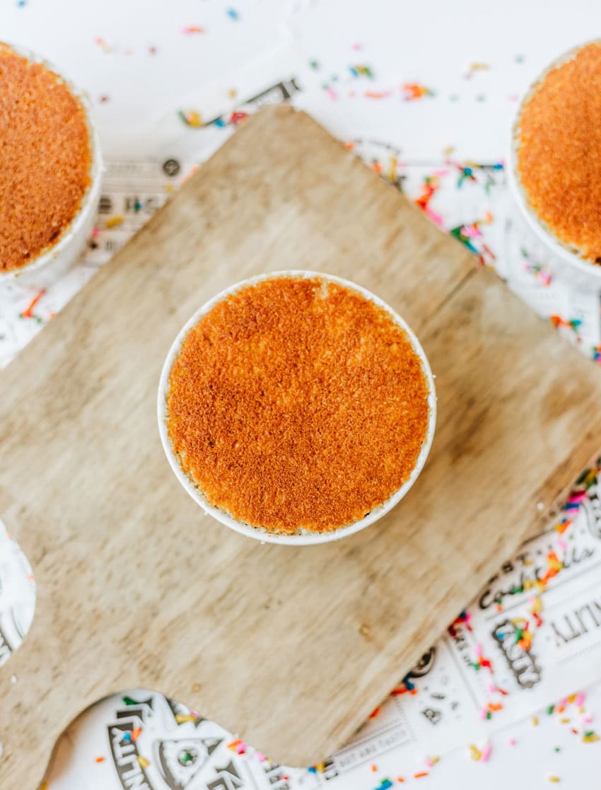a small white ramekin filled with yellow cake on a small wooden cutting board