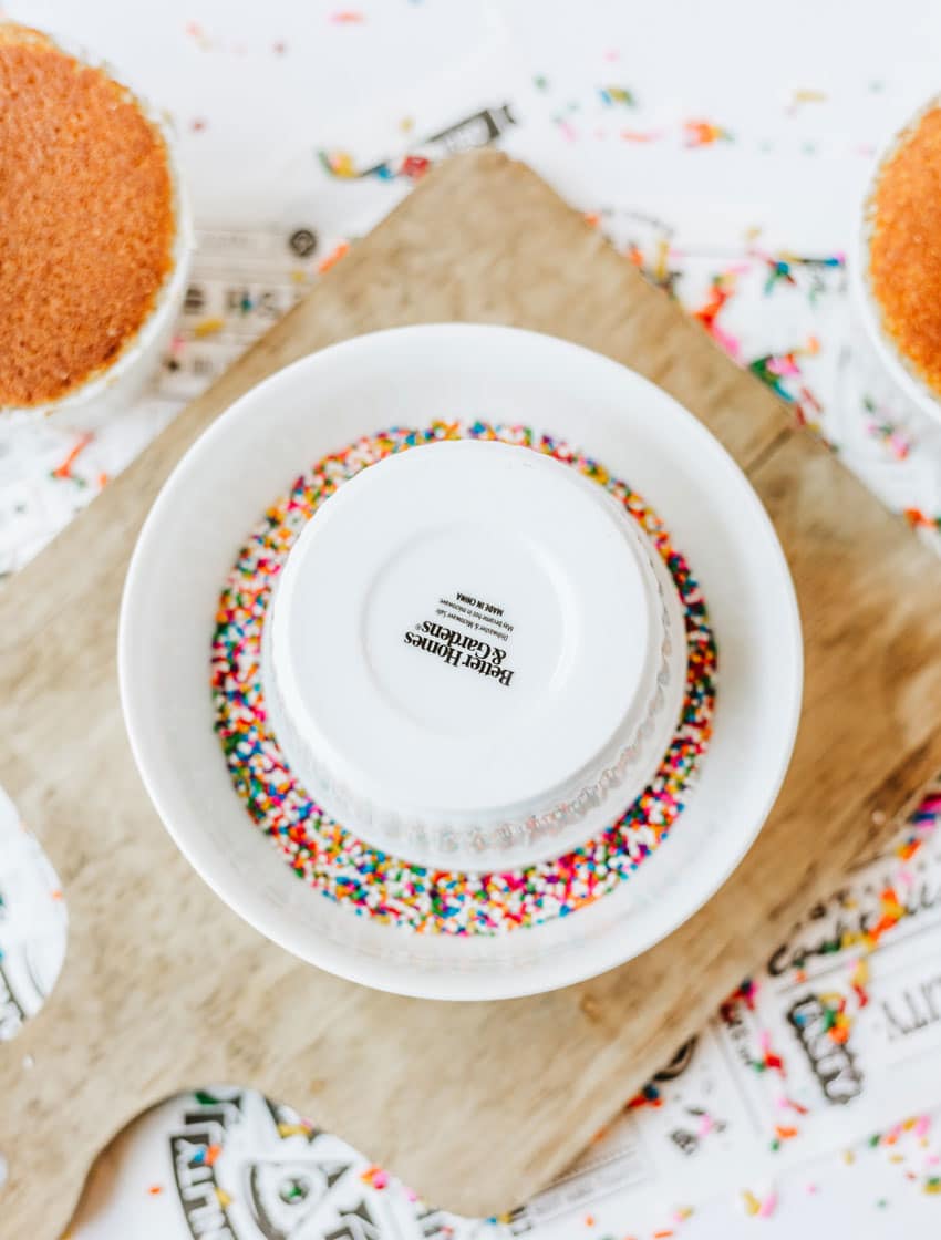 an upside down white ramekin in a small bowl filled with rainbow colored non pareill sprinkles
