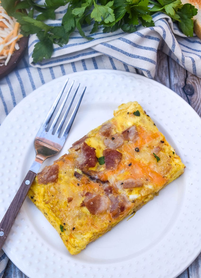 a slice of sheet pan breakfast casserole on a white plate with a fork resting on the side