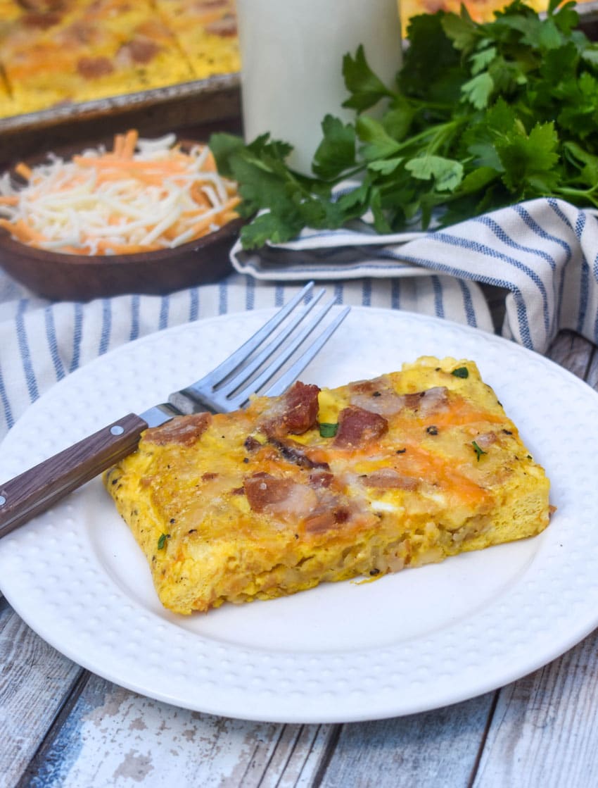 a slice of sheet pan breakfast casserole on a white plate with a fork resting on the side