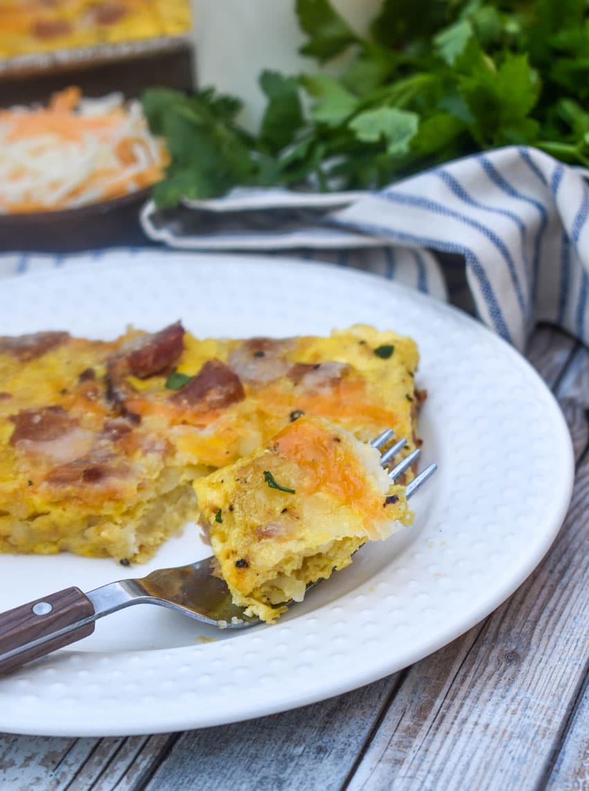 a fork holding a piece of a sheet pan breakfast casserole resting on the edge of a white plate