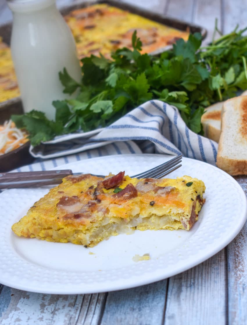 a slice of sheet pan breakfast casserole on a white plate with a fork resting on the side