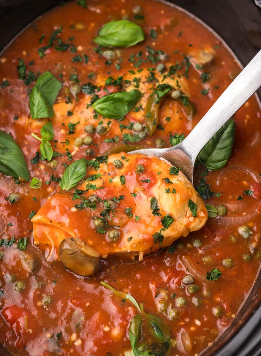 a silver spoon scooping a piece of Italian chicken cacciatore out of a black crock