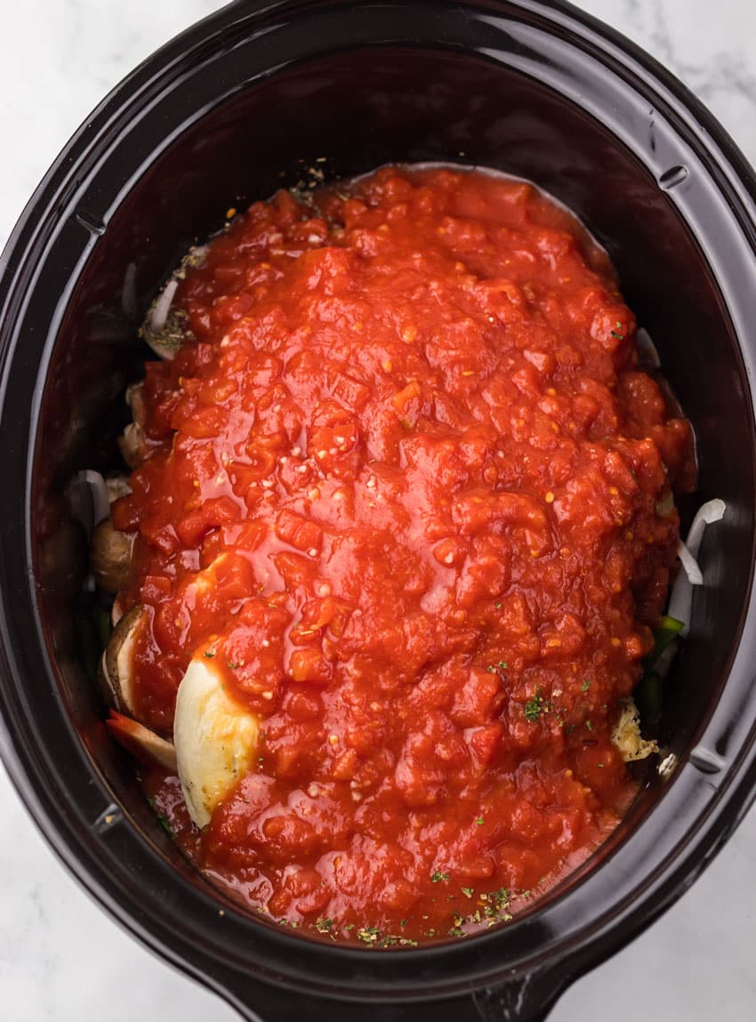 crushed tomatoes and dried herbs over chicken in the black bowl of a slow cooker