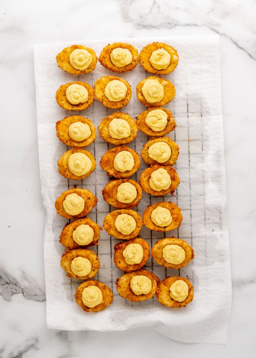 deep fried deviled eggs arranged in rows on a paper towel lined wire rack