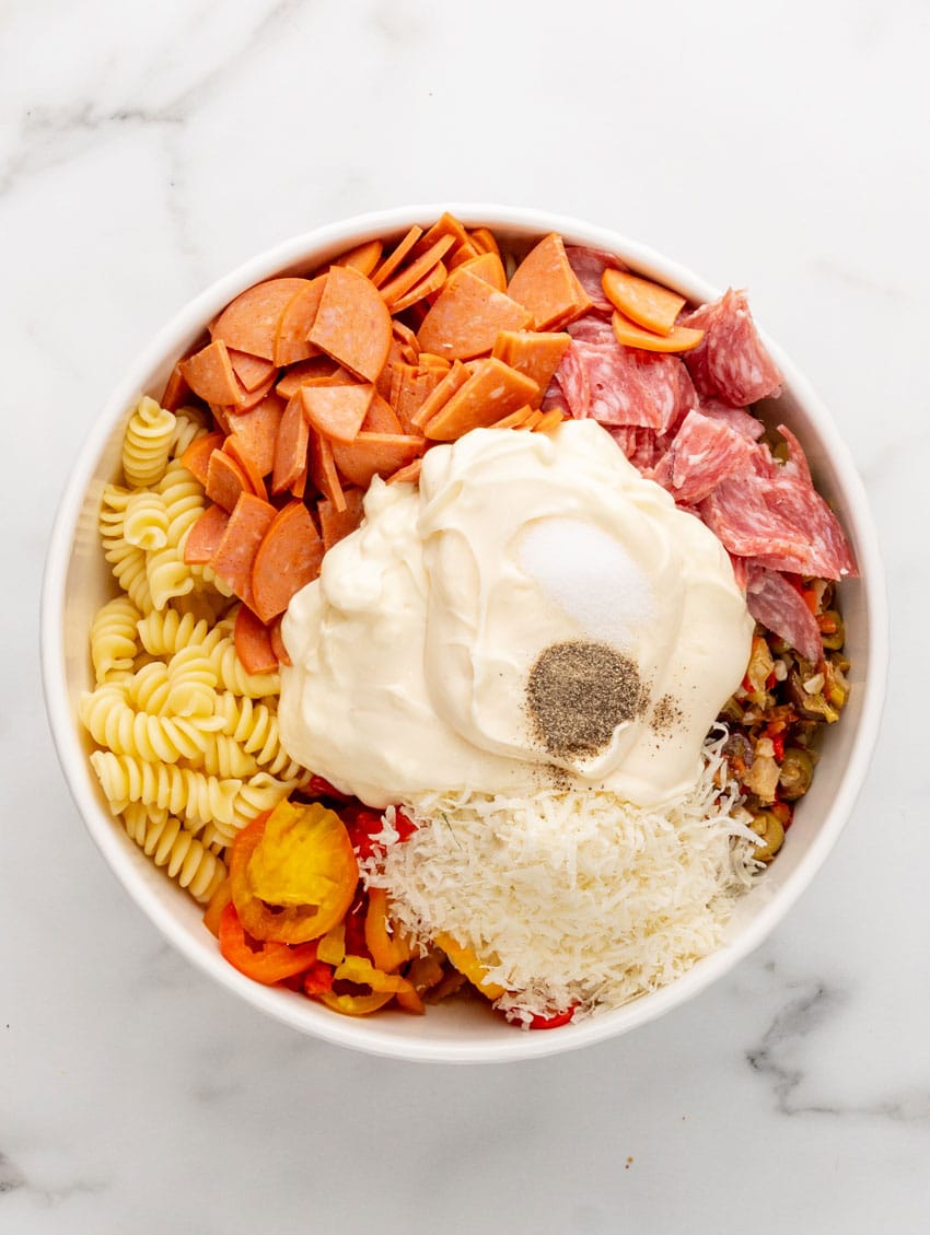 muffuletta salad ingredients and cooked pasta in a white mixing bowl