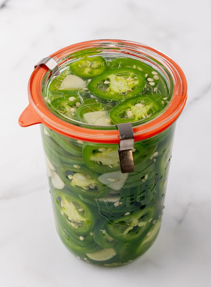 thinly sliced jalapeno peppers and slices of fresh garlic marinating in brine in a small glass jar