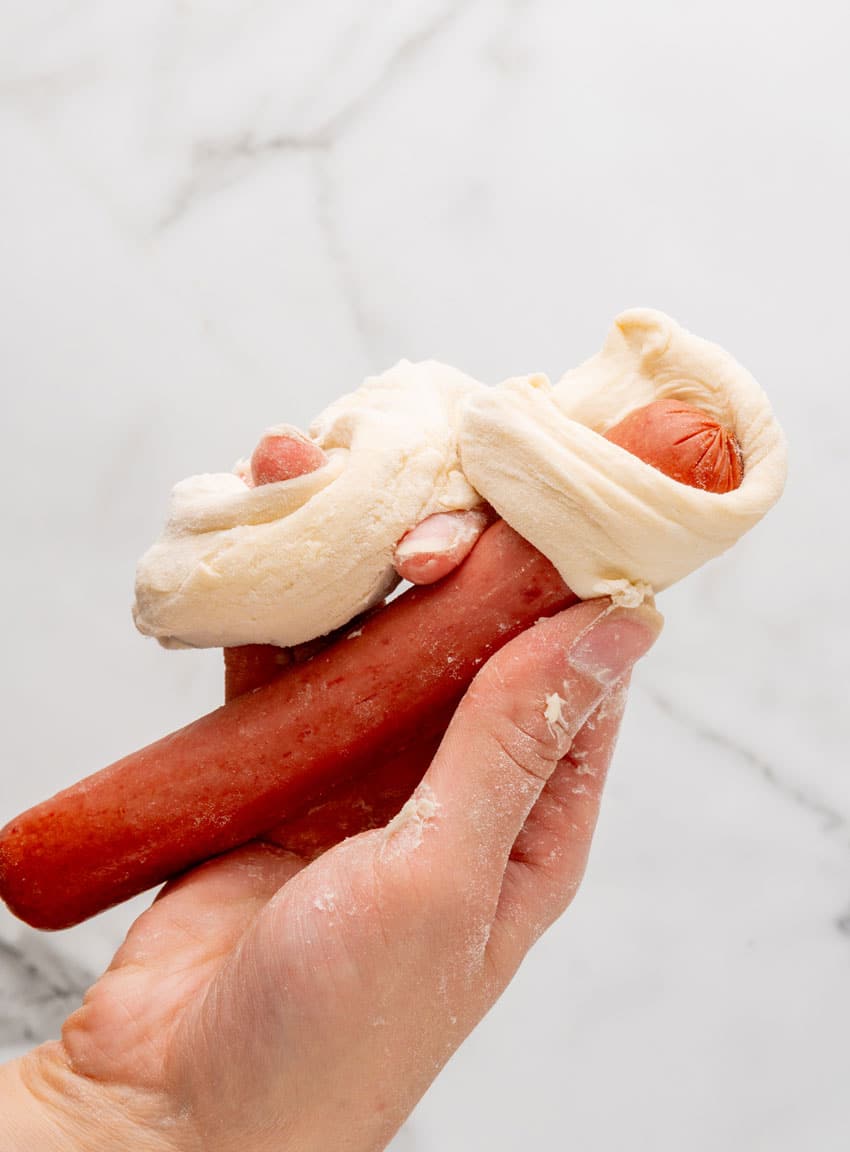 pretzel dough being wrapped around an uncooked all beef hot dog