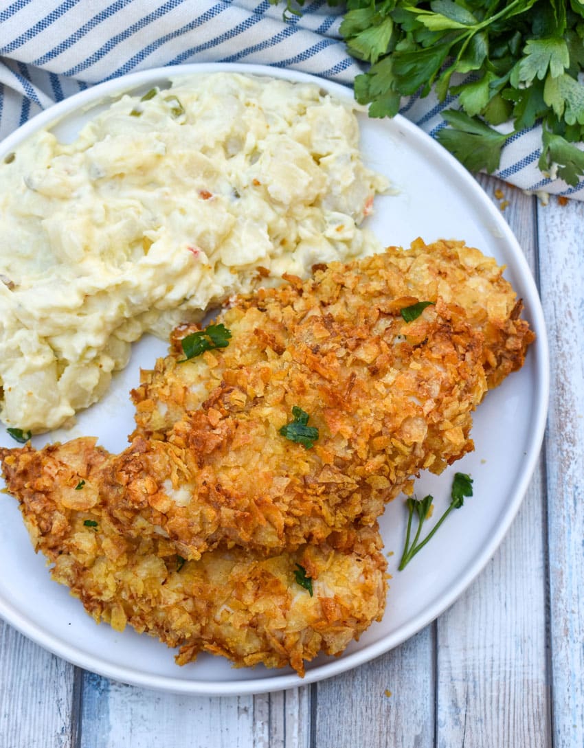 air fryer potato chip chicken tenders stacked on a white plate with potato salad on the side