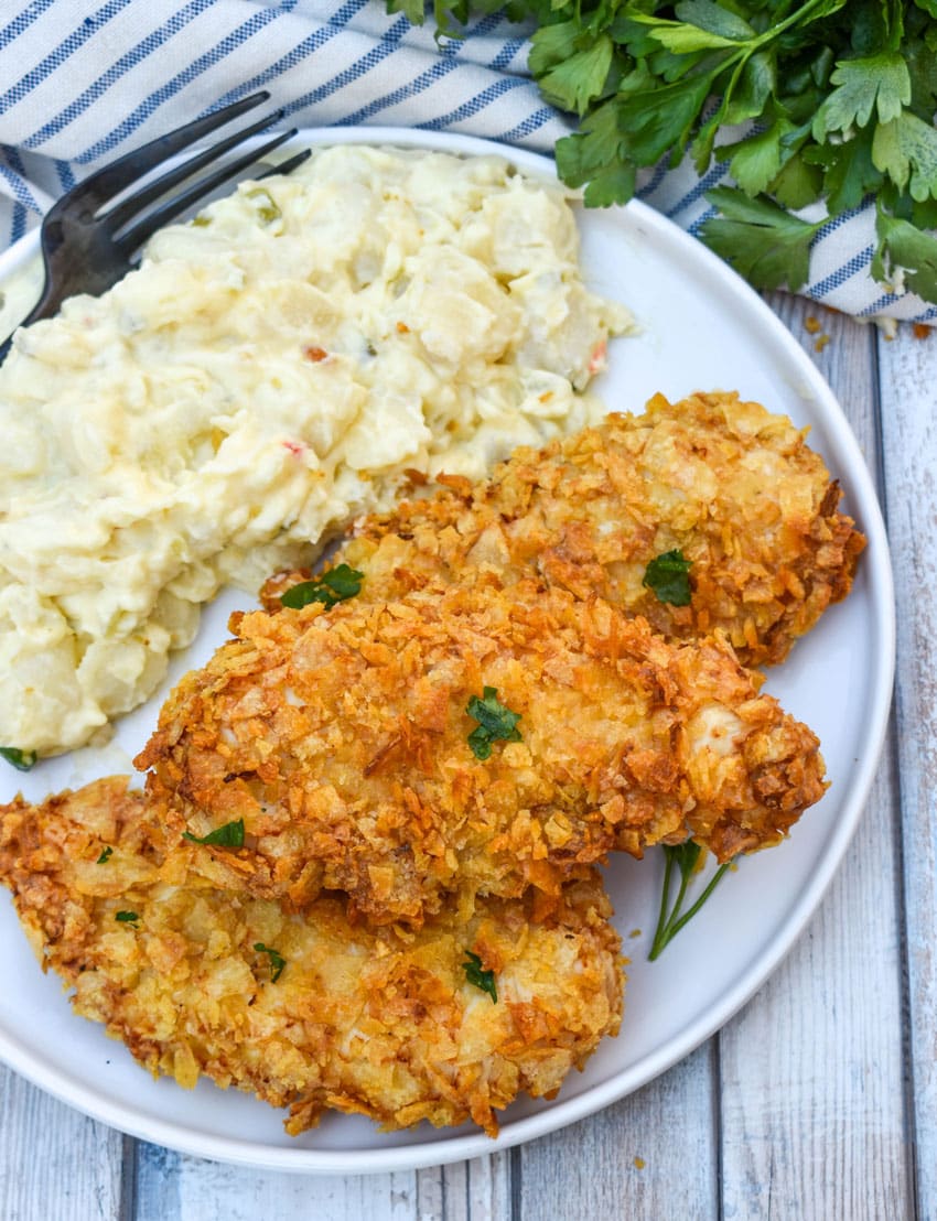 air fryer potato chip chicken tenders stacked on a white plate with potato salad on the side