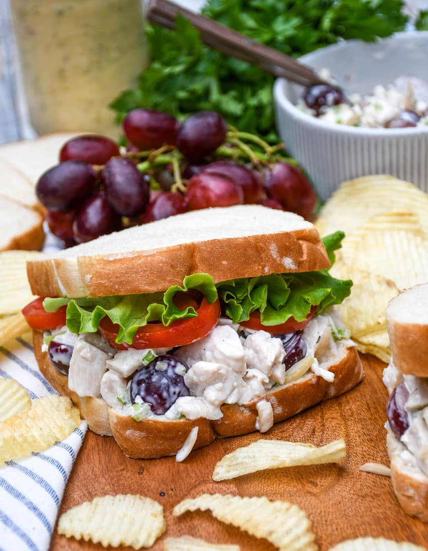 copycat napa chicken salad sandwich on a wooden cutting board with chips on the side