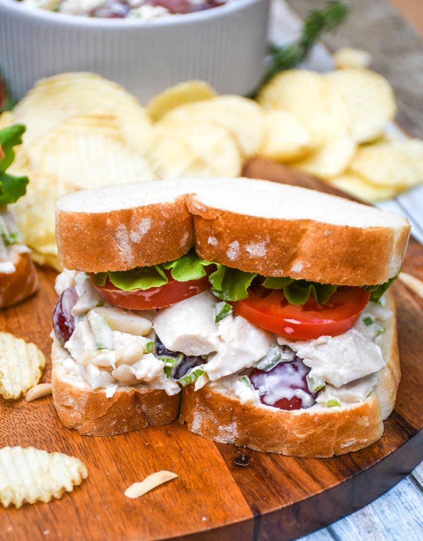 copycat napa chicken salad sandwich on a wooden cutting board with chips on the side