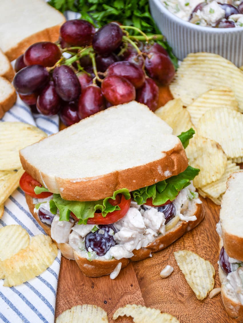 copycat napa chicken salad sandwich on a wooden cutting board with chips on the side
