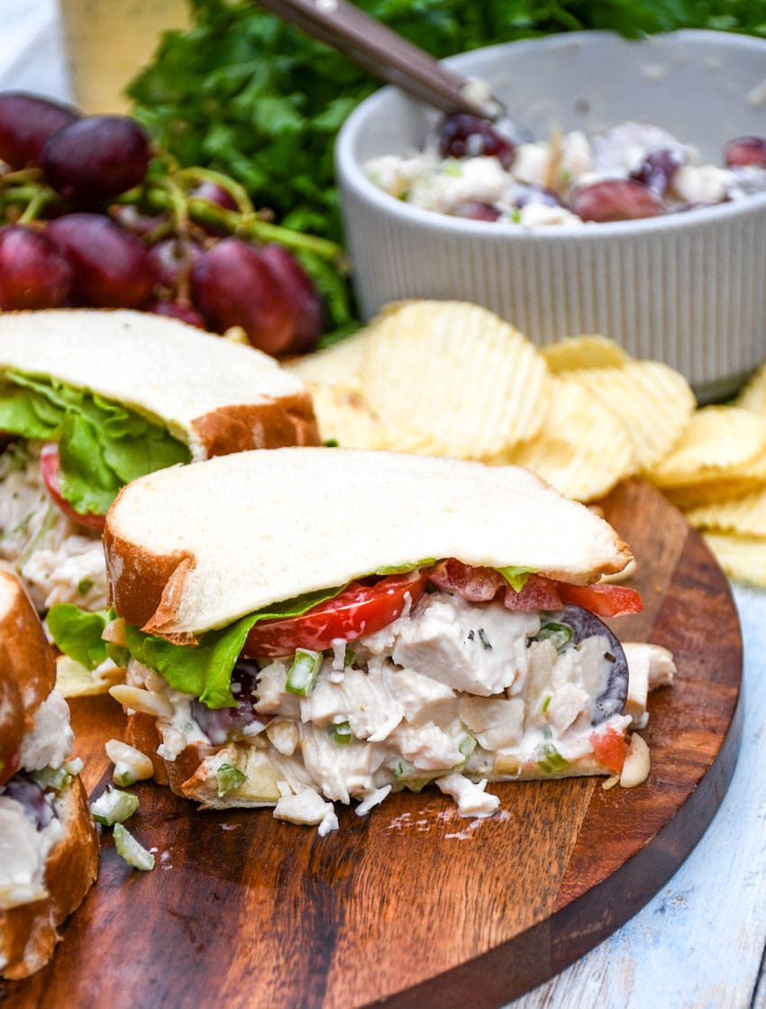 copycat napa chicken salad sandwich on a wooden cutting board with chips on the side
