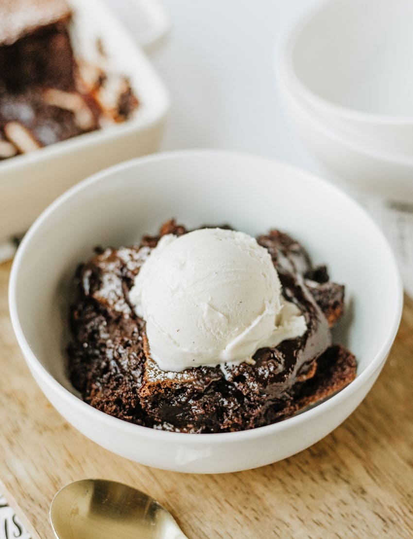 ina garten's brownie pudding topped with a scoop of vanilla ice cream in a white bowl
