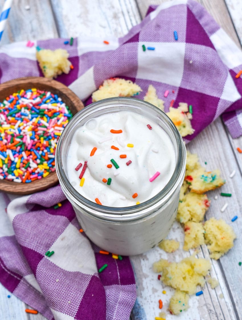 a funfetti cake milkshake topped with rainbow sprinkles in a small glass jar