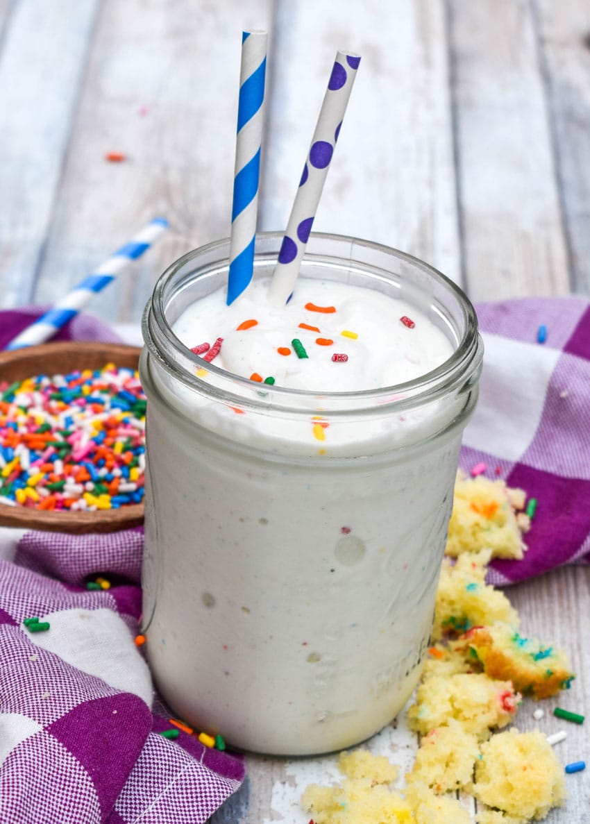 a funfetti cake milkshake topped with rainbow sprinkles in a small glass jar