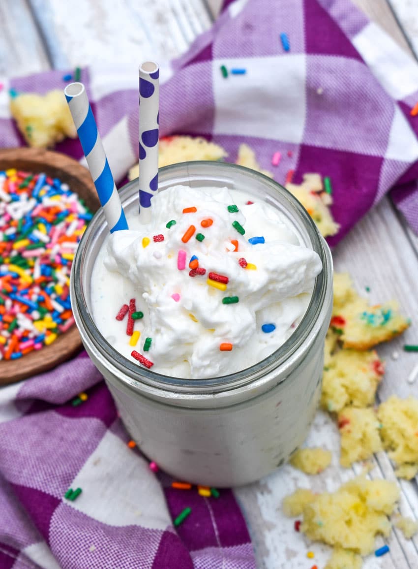 a funfetti cake milkshake topped with rainbow sprinkles in a small glass jar