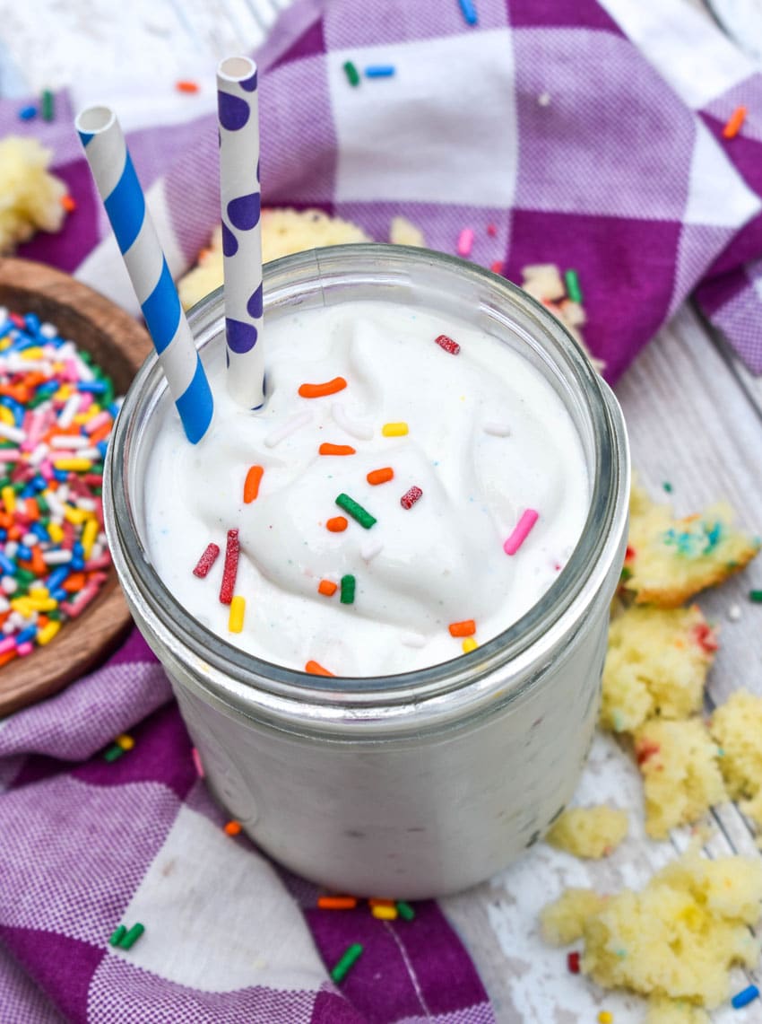 a funfetti cake milkshake topped with rainbow sprinkles in a small glass jar