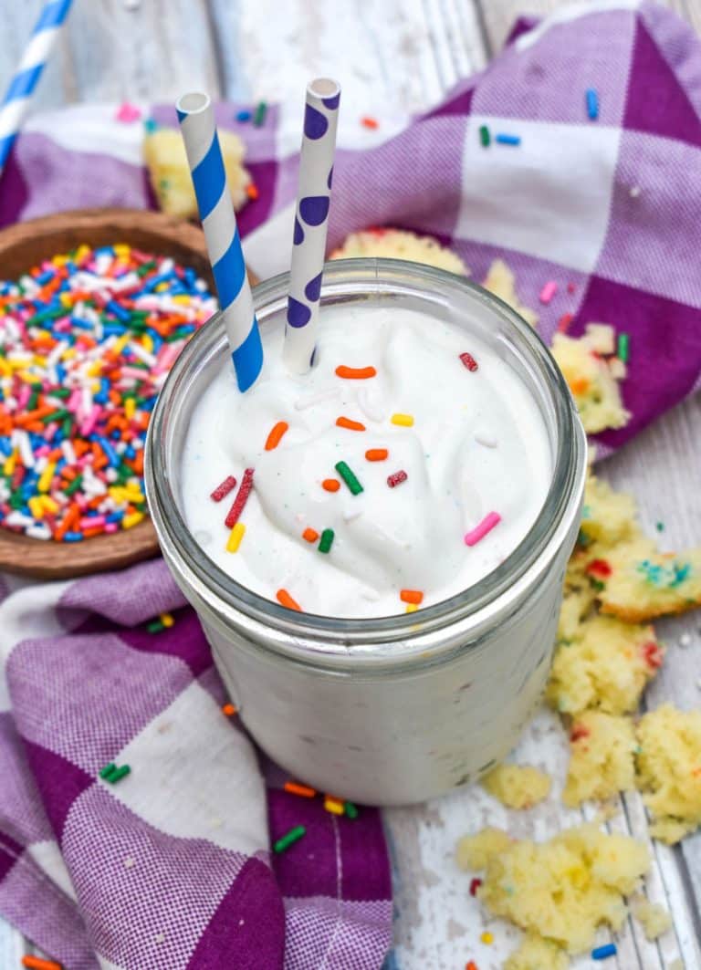 a funfetti cake milkshake topped with rainbow sprinkles in a small glass jar