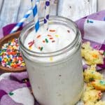 a funfetti cake milkshake topped with rainbow sprinkles in a small glass jar