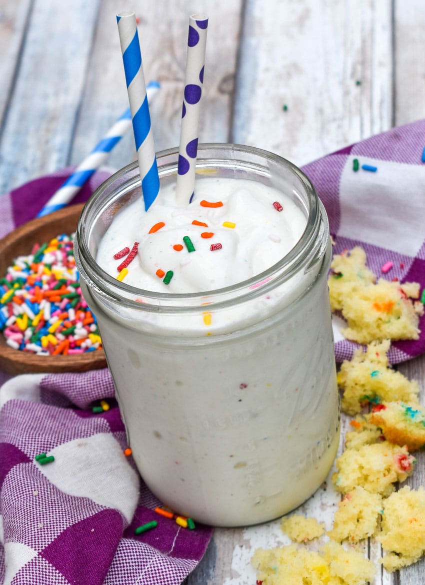 a funfetti cake milkshake topped with rainbow sprinkles in a small glass jar