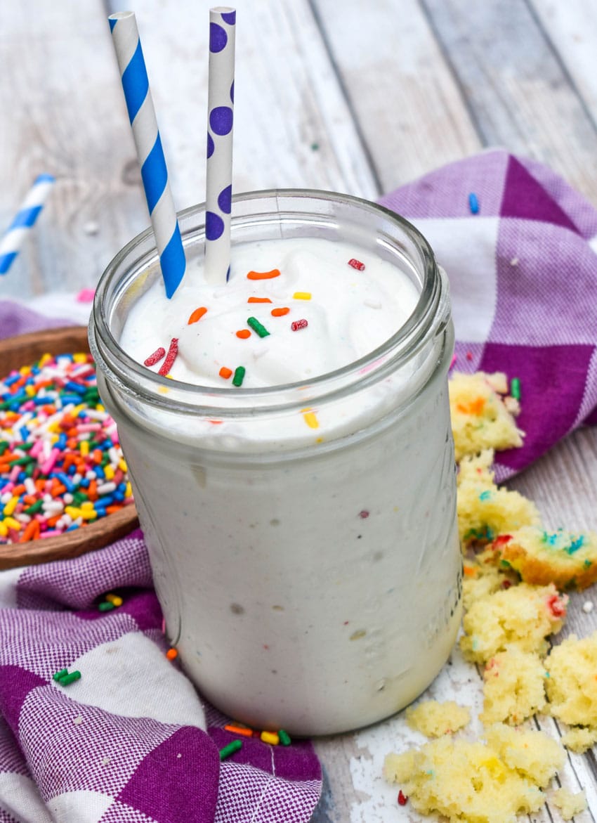 a funfetti cake milkshake topped with rainbow sprinkles in a small glass jar