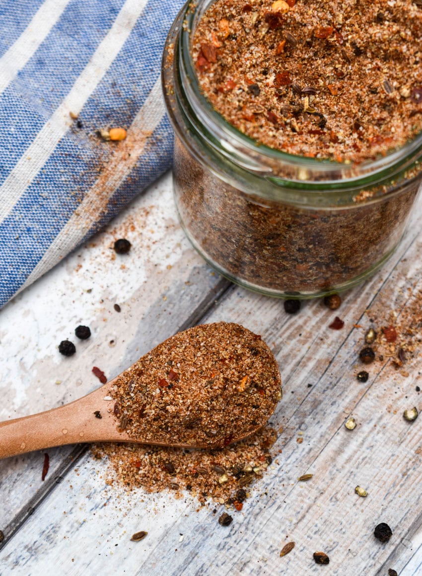 a wooden spoon holding homemade montreal steak seasoning resting on a wooden table