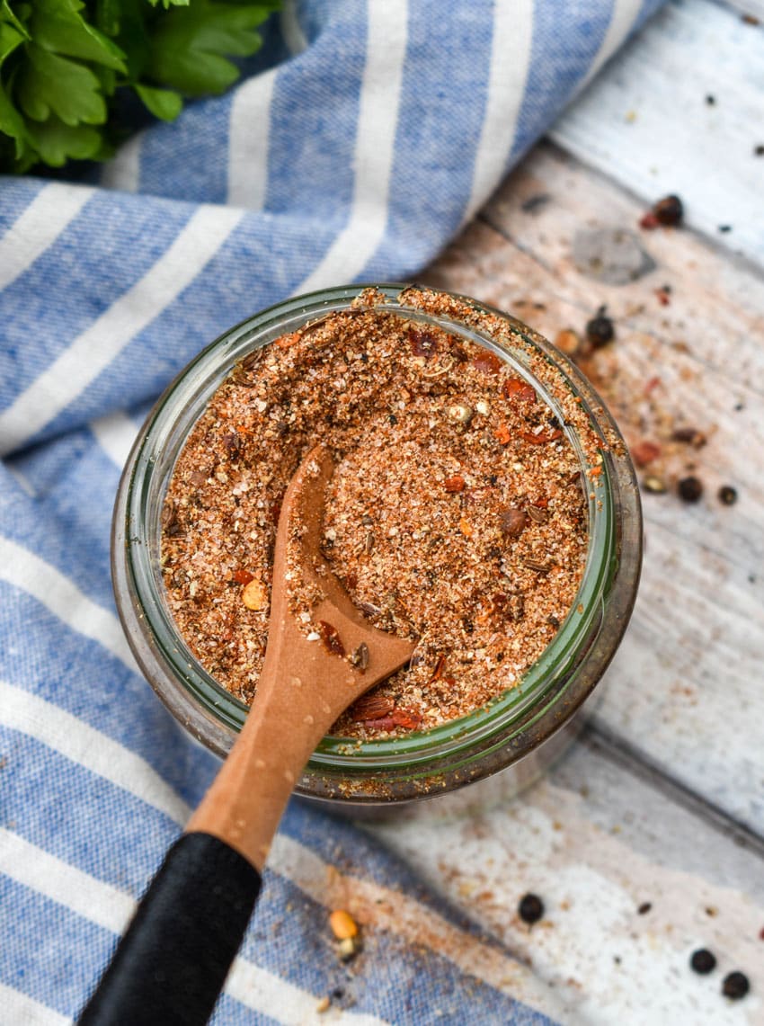 a small wooden spoon scooping homemade montreal steak seasoning out of a small glass jar