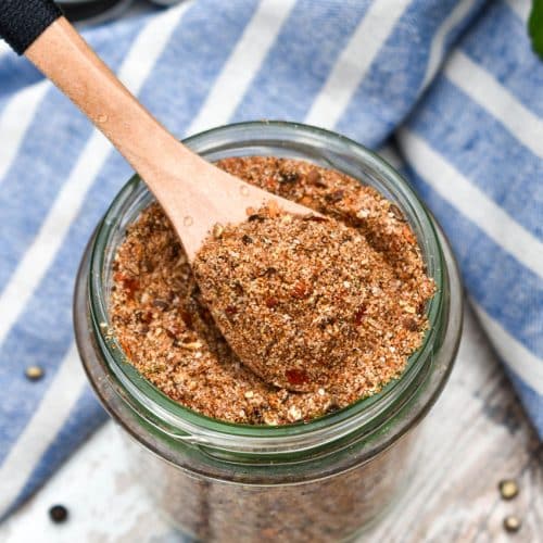 a small wooden spoon scooping homemade montreal steak seasoning out of a small glass jar