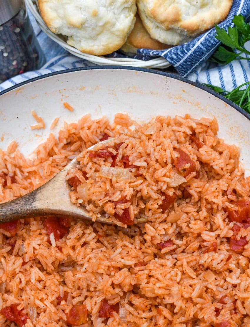a wooden spoon scooping southern tomatoes and rice out of a cast iron skillet