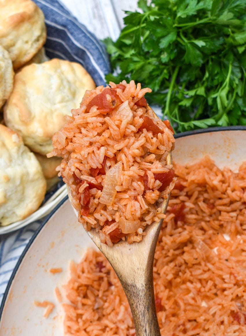 a wooden spoon holding up a scoop of southern tomatoes and rice