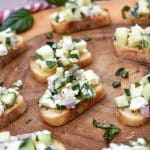 zucchini bruschetta on toasted baguette slices on a wooden cutting board