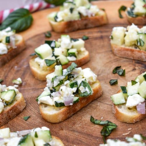 zucchini bruschetta on toasted baguette slices on a wooden cutting board