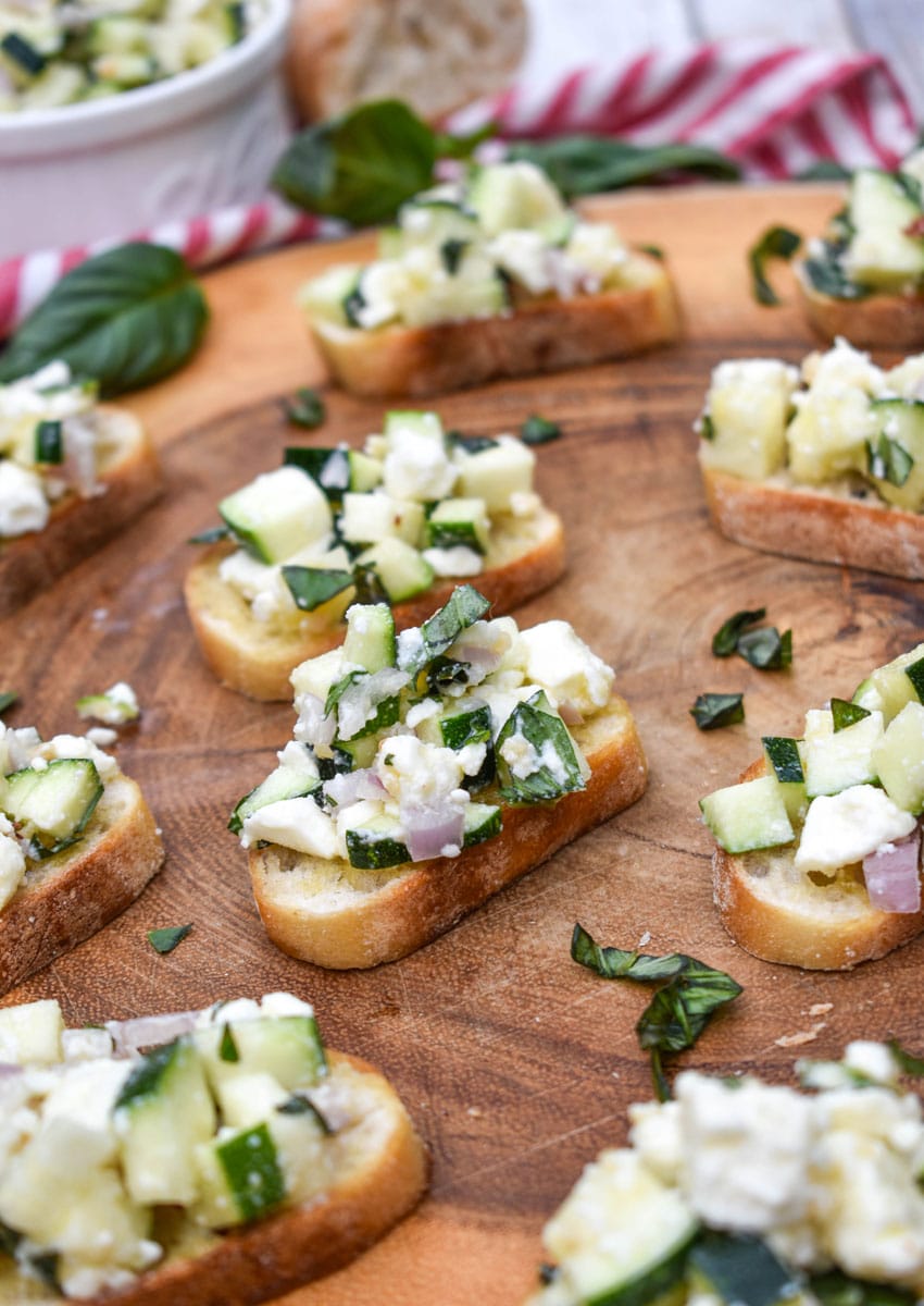 zucchini bruschetta on toasted baguette slices on a wooden cutting board
