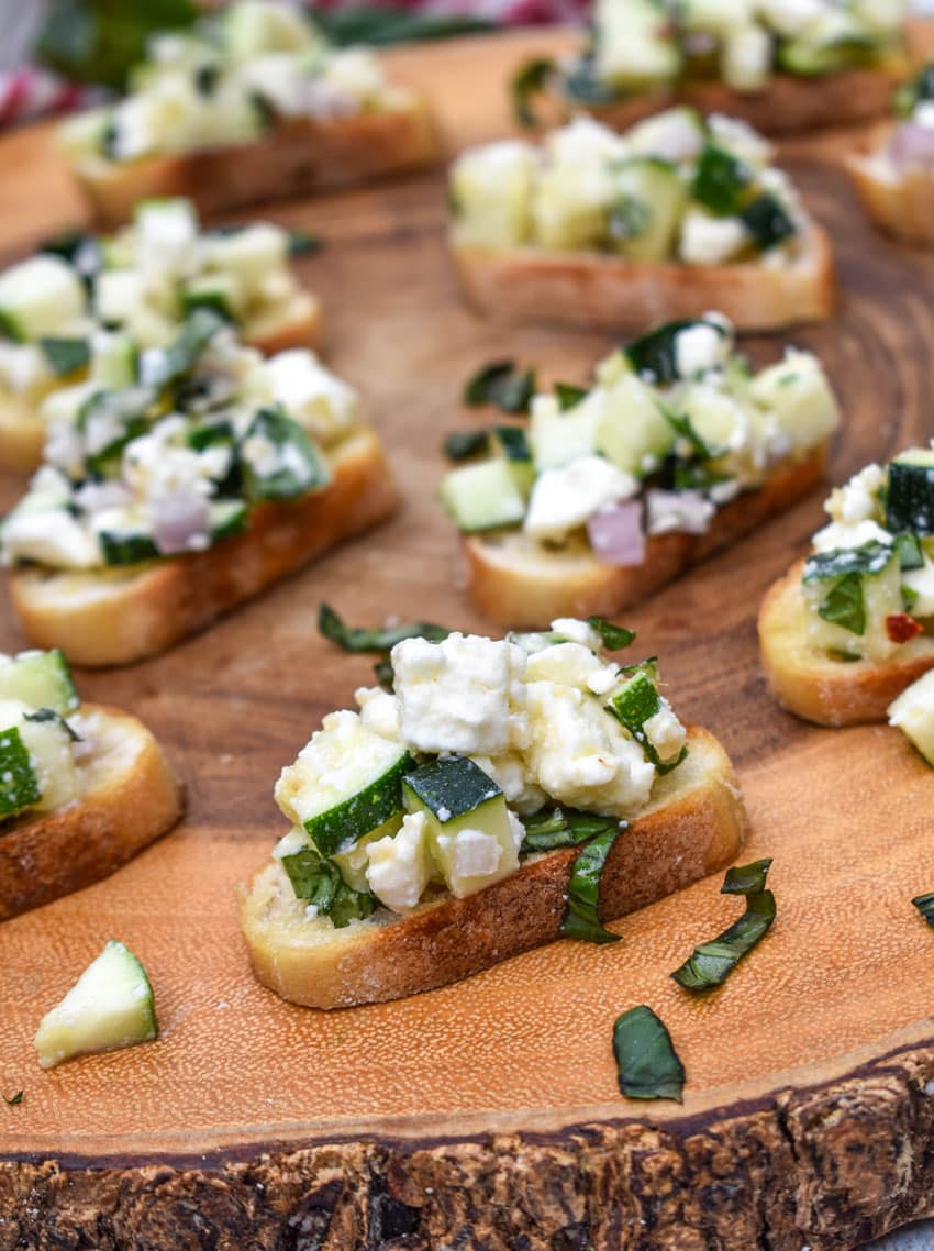 zucchini bruschetta on toasted baguette slices on a wooden cutting board
