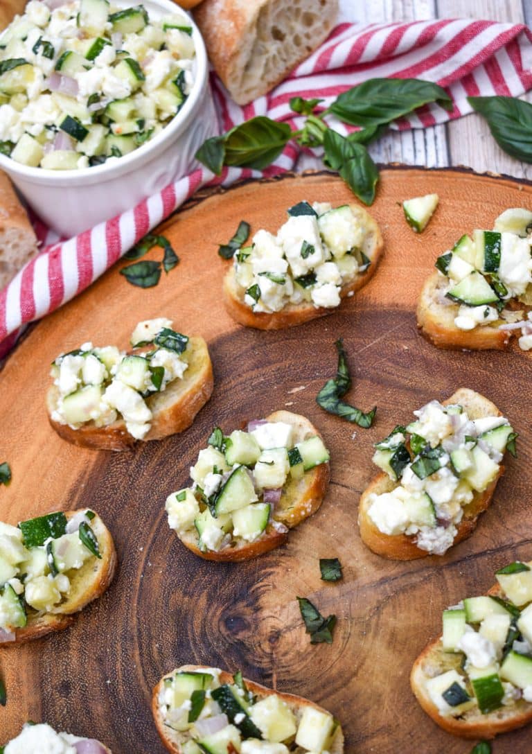 zucchini bruschetta on toasted baguette slices on a wooden cutting board