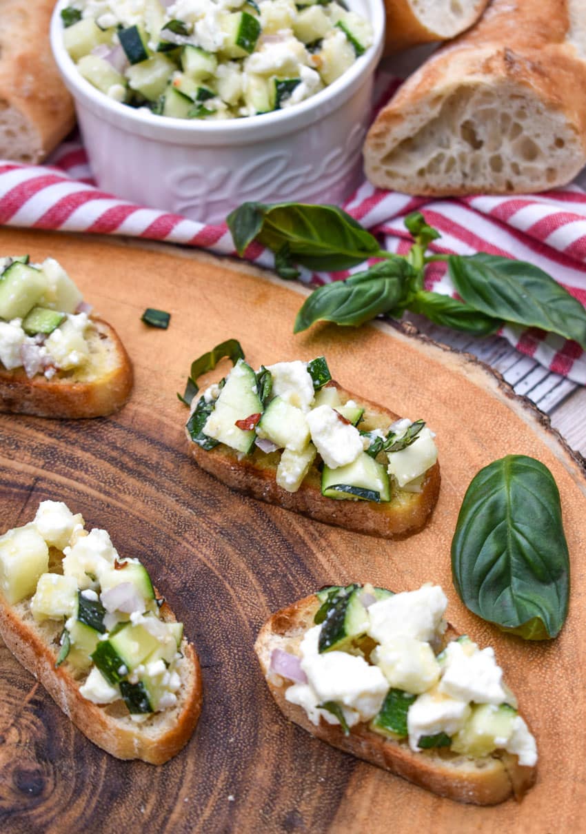 zucchini bruschetta on toasted baguette slices on a wooden cutting board