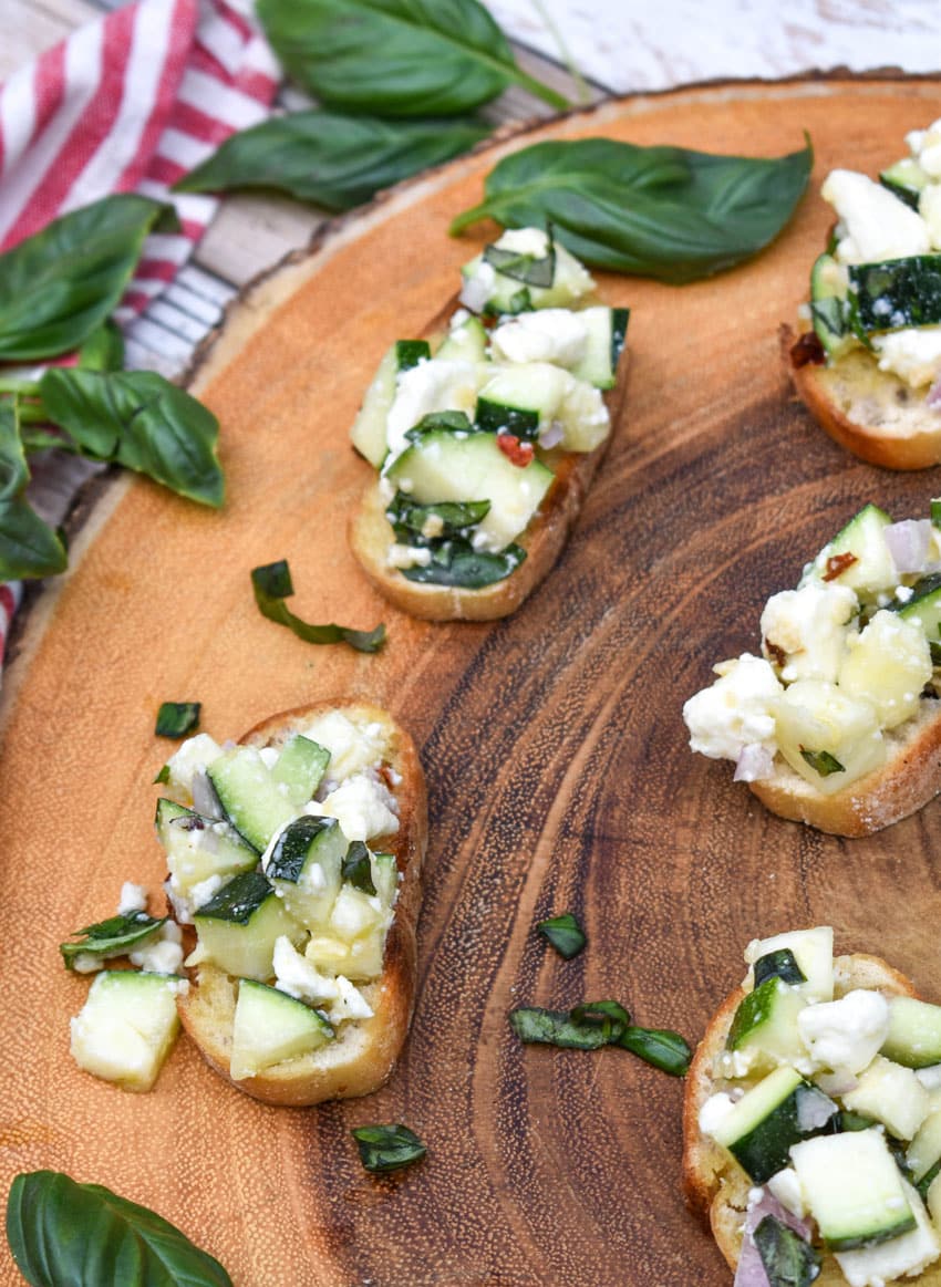 zucchini bruschetta on toasted baguette slices on a wooden cutting board