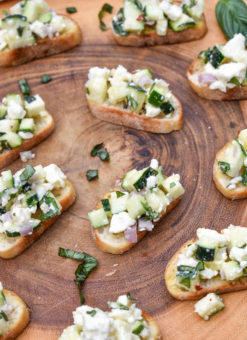 zucchini bruschetta on toasted baguette slices on a wooden cutting board